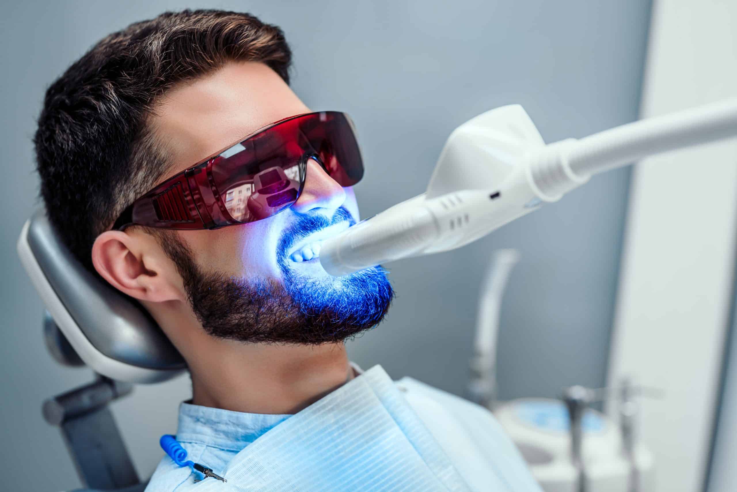 man sitting in dental chair with light on his teeth getting whitening treatment at the dentist