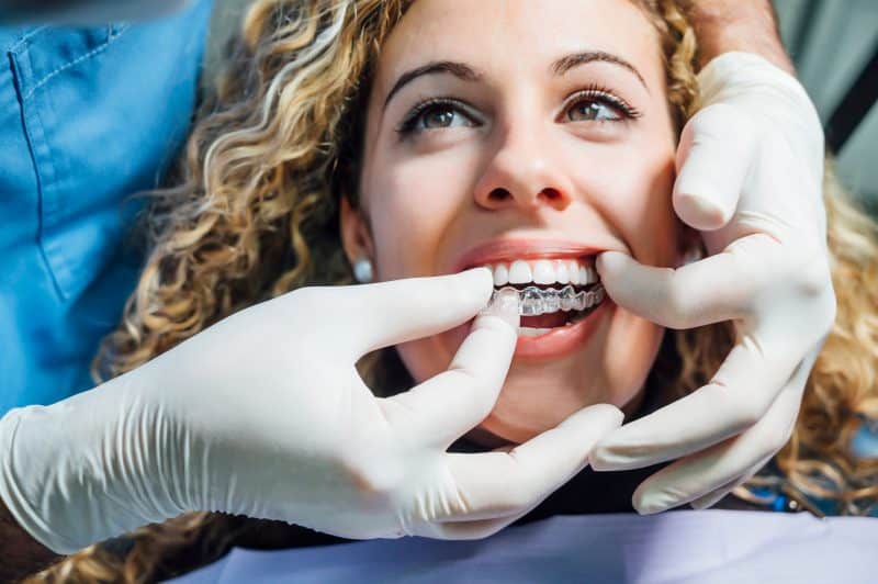 doctor putting clear aligner into mouth of blonde woman