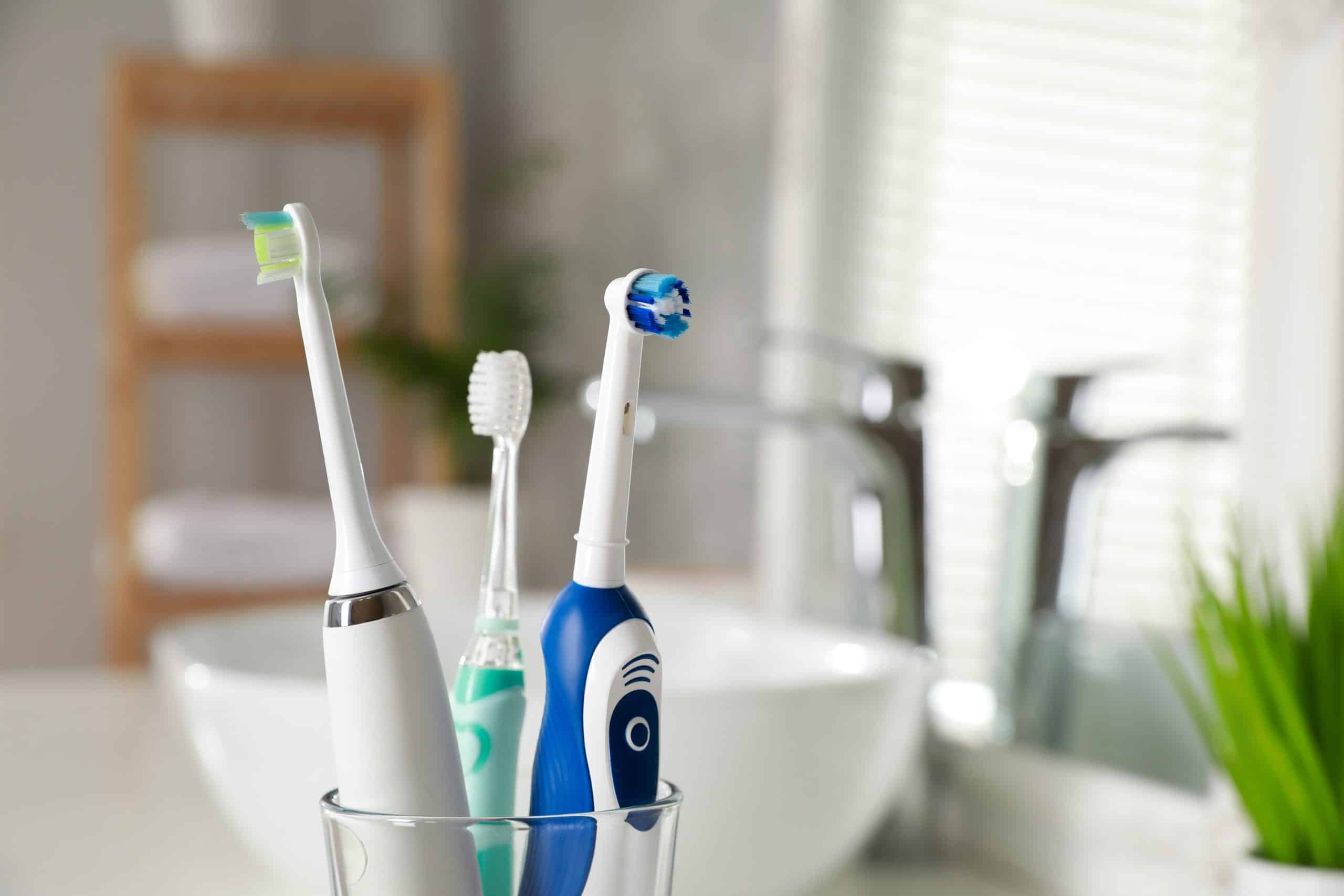 three toothbrushes in a glass next to bathroom sink