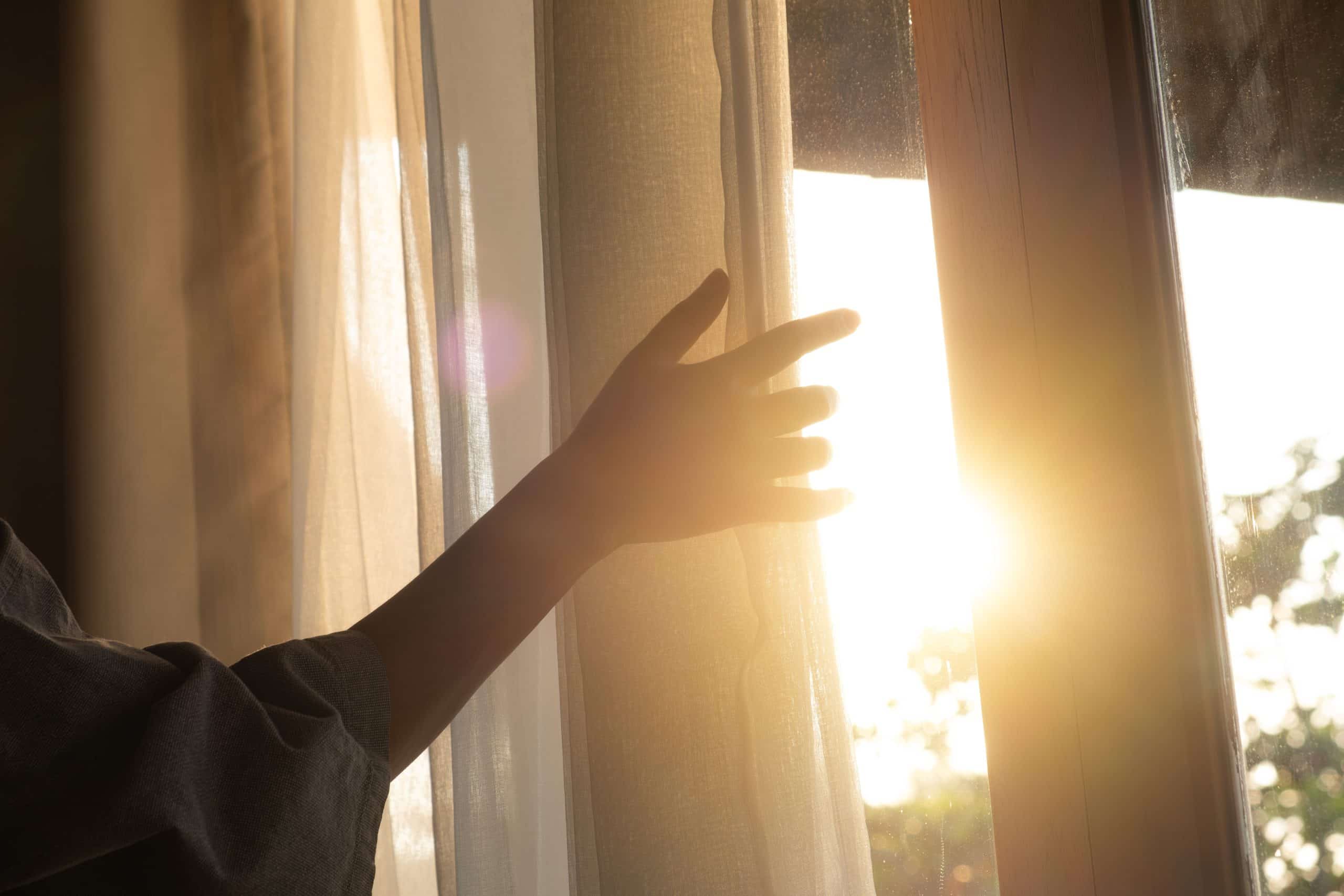 Woman’s hand pulling back curtain at sunrise