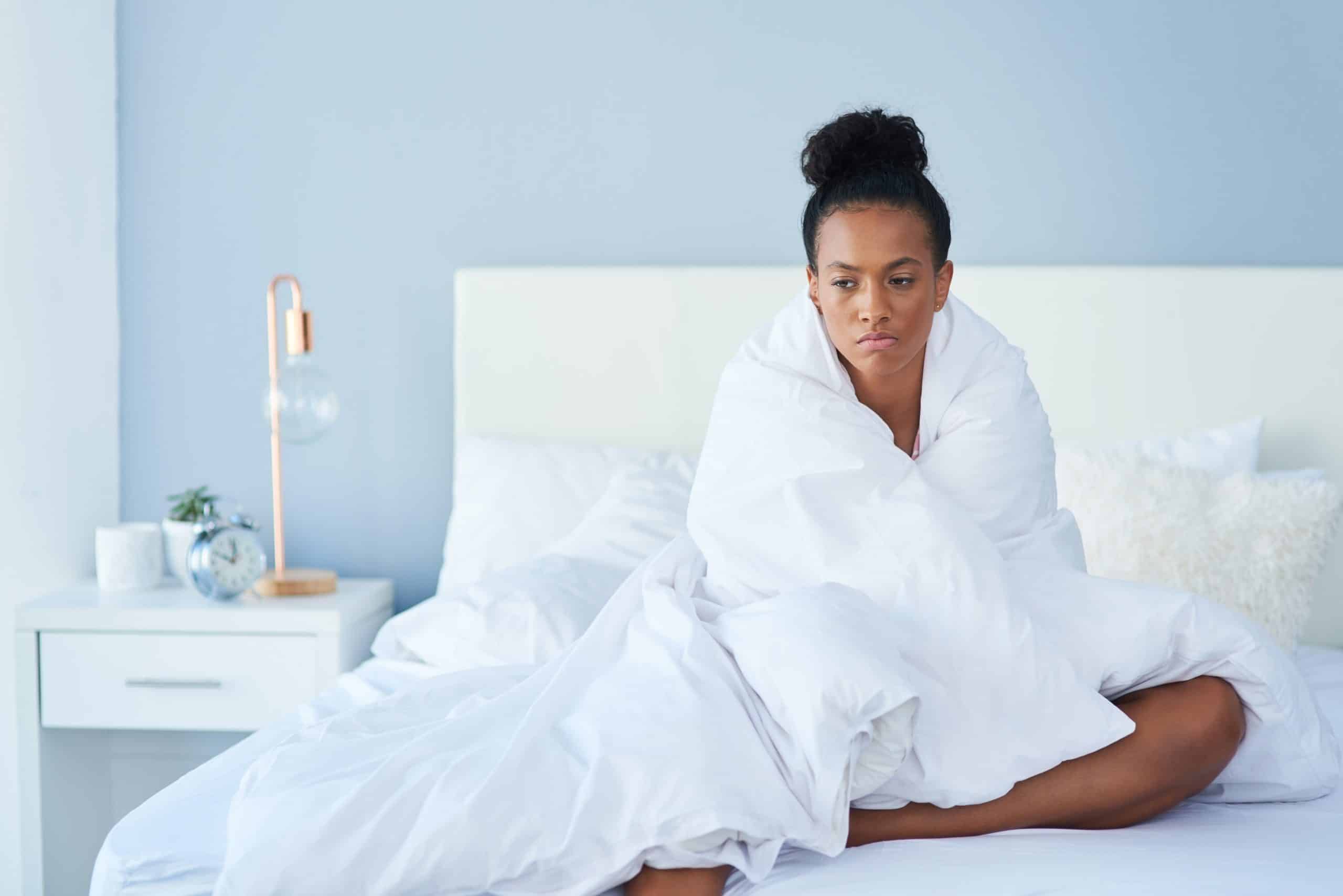 grumpy woman wrapped in white blanket sits in bed