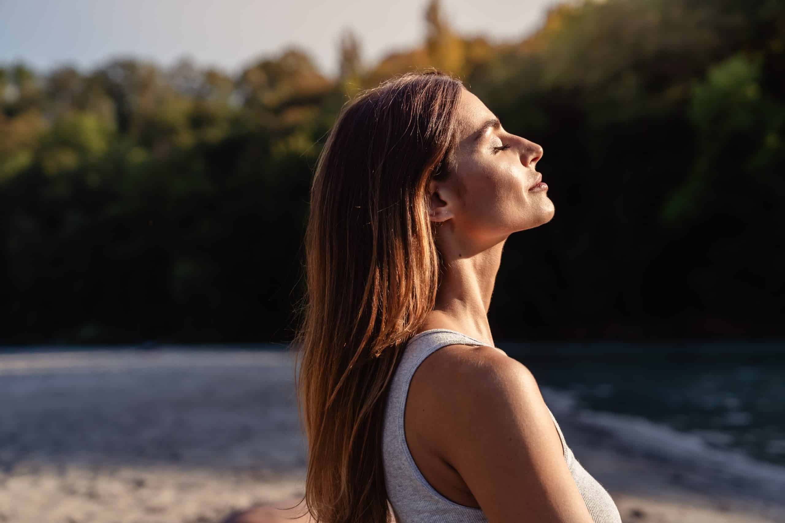 woman with long hair sits with eyes closed tilting her face toward the sun