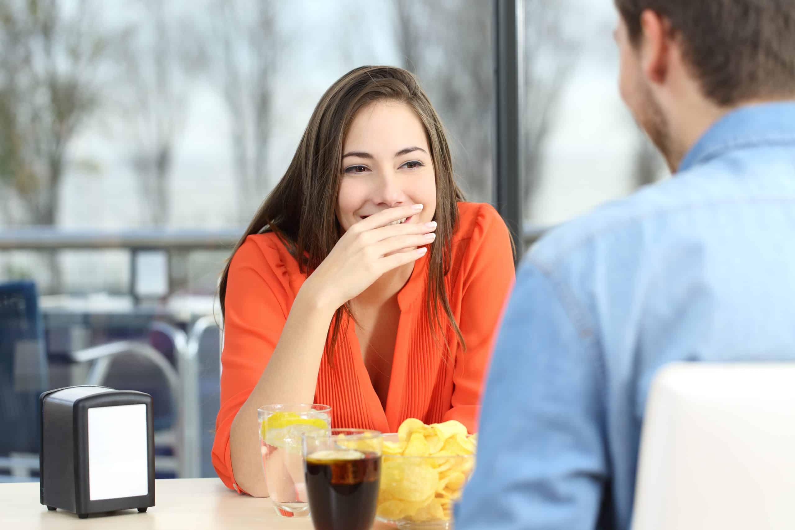 Woman sitting across from a man covers her mouth while smiling