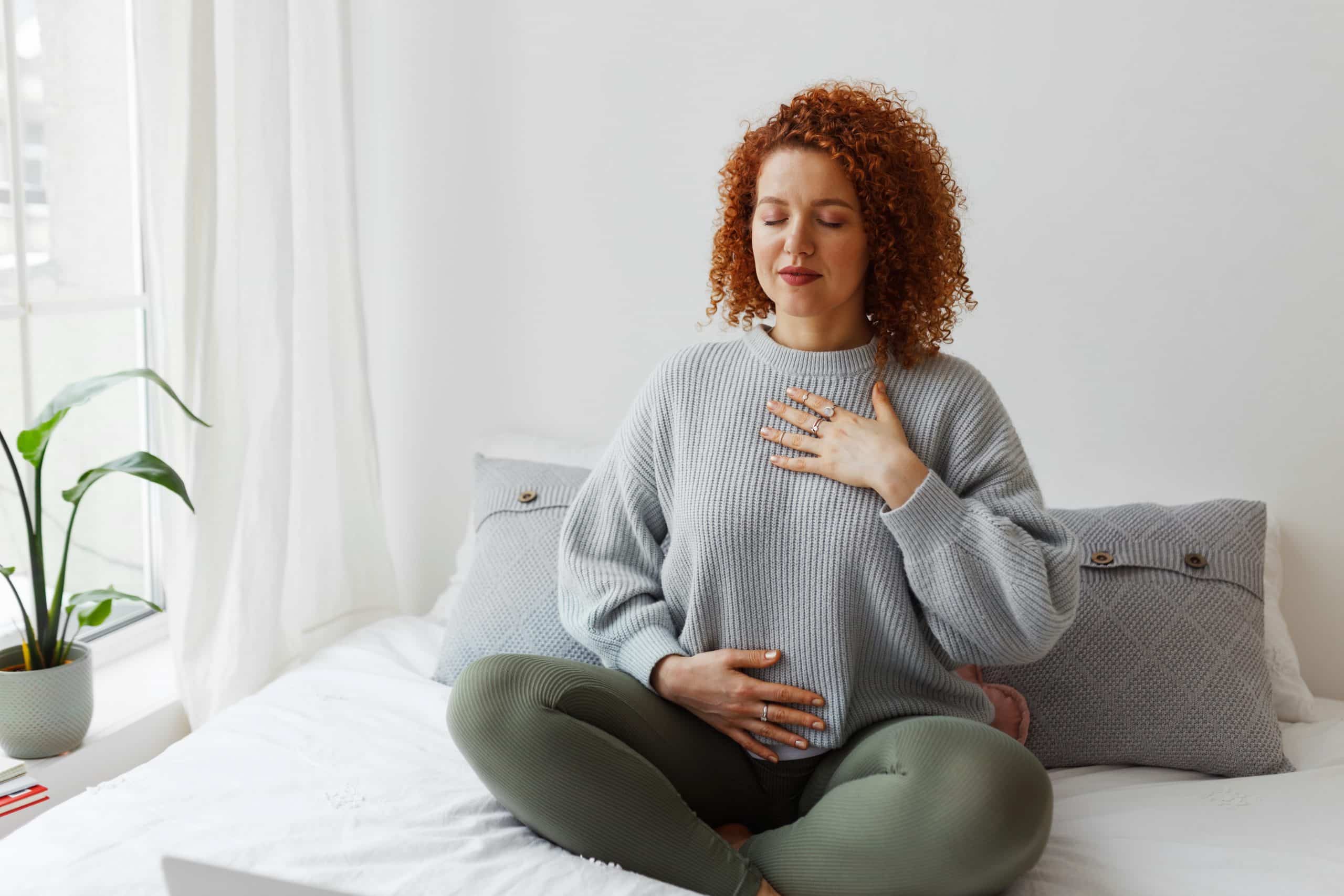 woman with curly red hair sitting on bed breathing deeply