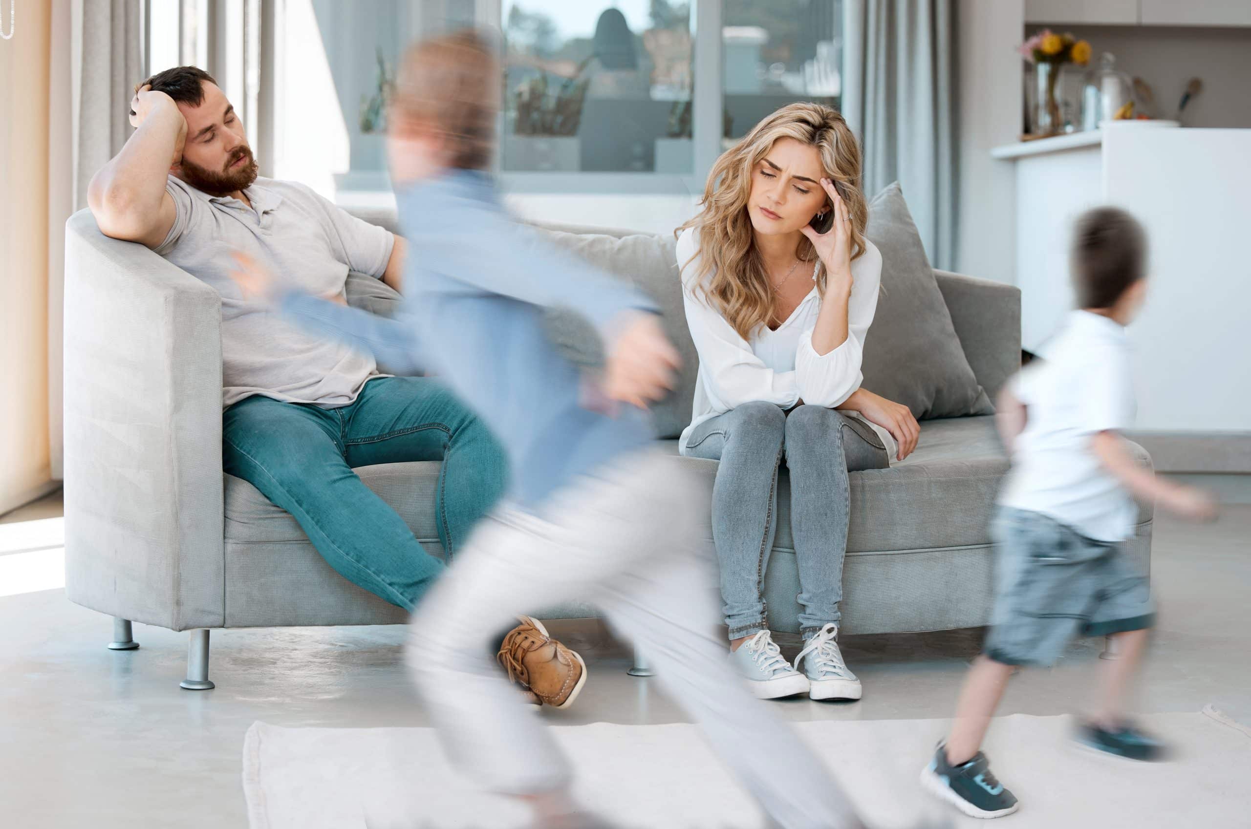 stressed parents watch kids run around from couch