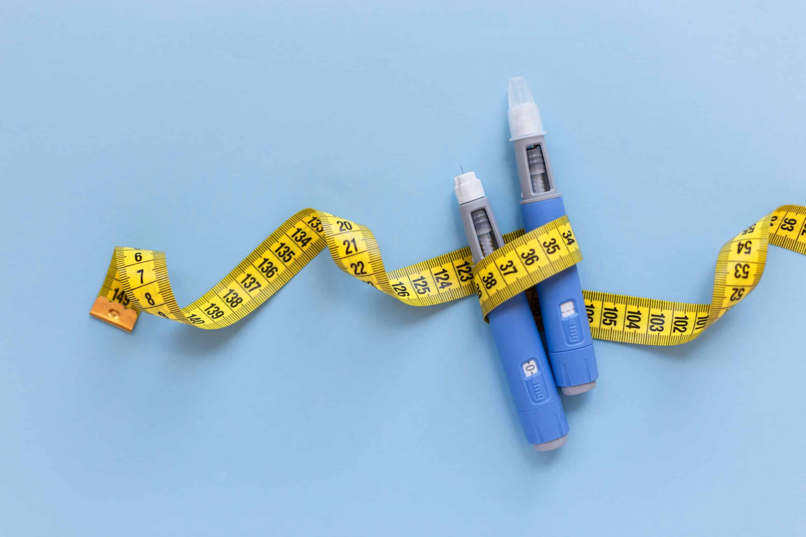 tape measure wrapped around GLP-1 injectors on blue background