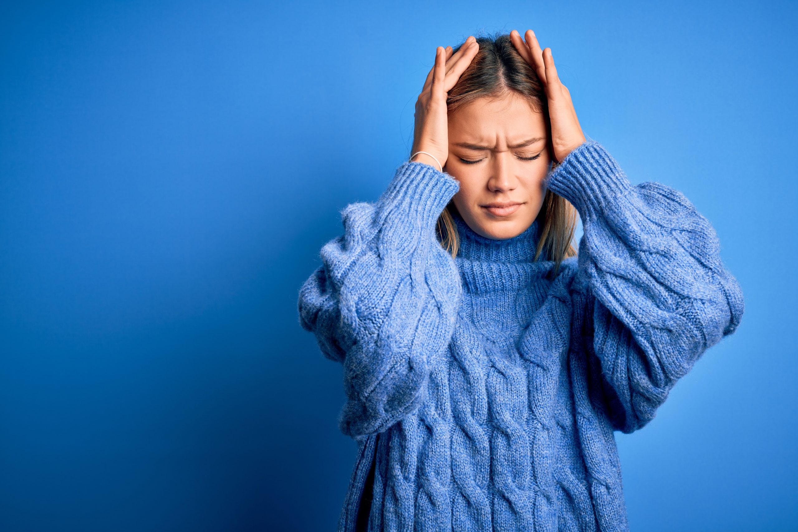 woman in blue sweater holds head in pain