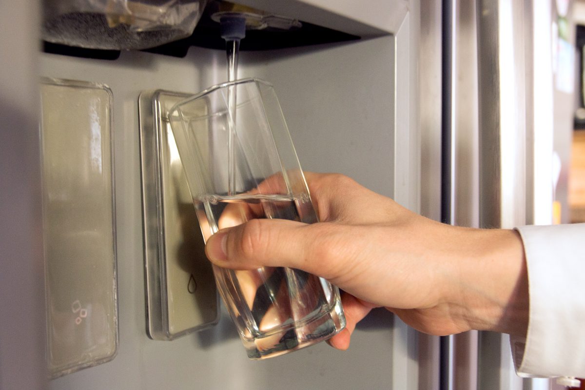 man's hand filling a glass with water from refrigerator spout