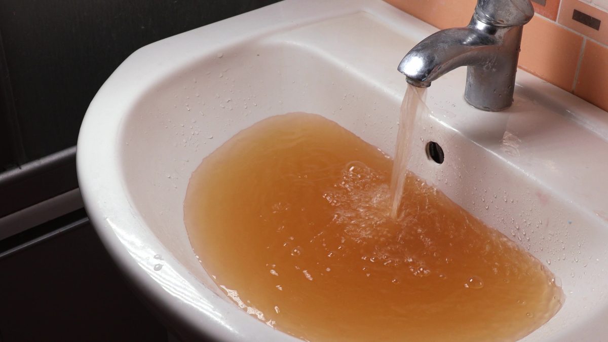 rusty brown water pours into a sink from bathroom tap