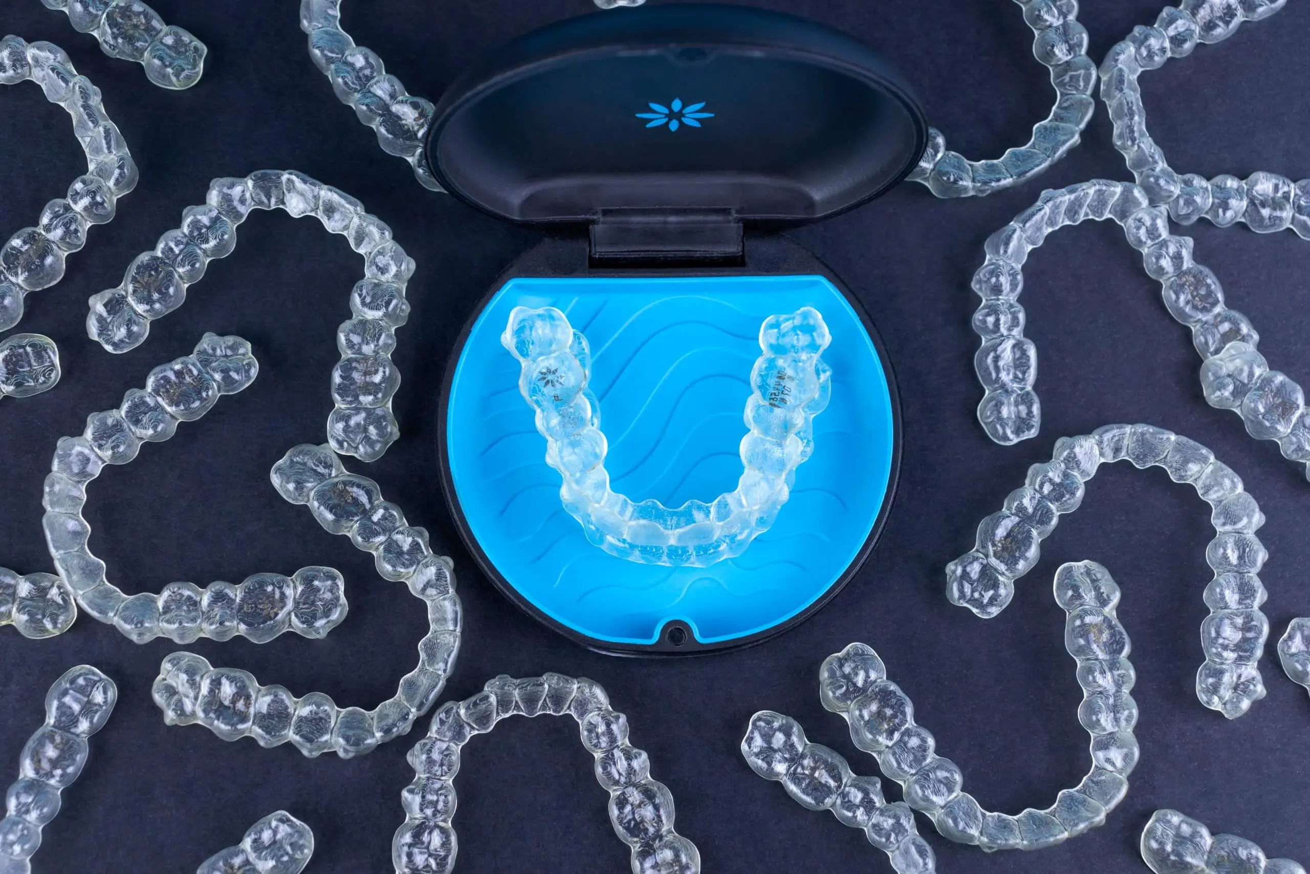 Clear Invisalign aligner surrounded by individual tooth trays